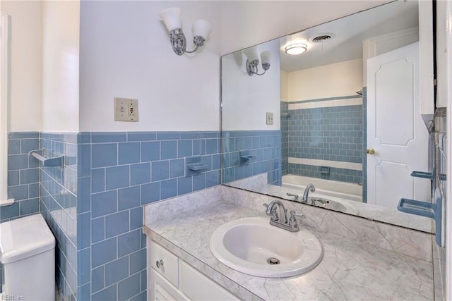 full bathroom with visible vents, wainscoting, vanity, and tile walls