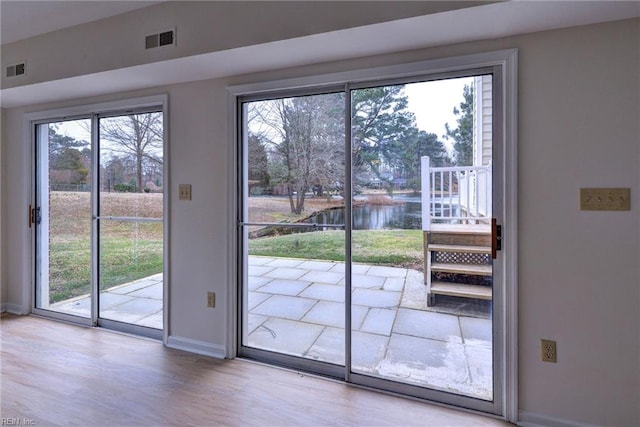 doorway featuring a wealth of natural light, a water view, visible vents, and baseboards