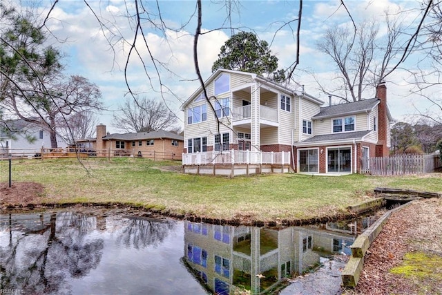 rear view of house featuring a balcony, brick siding, fence, a lawn, and a chimney