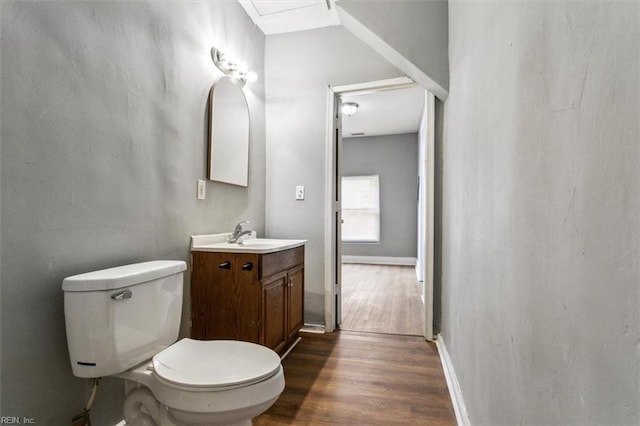 half bath with baseboards, vanity, toilet, and wood finished floors