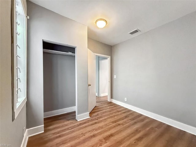 unfurnished bedroom featuring visible vents, a closet, baseboards, and wood finished floors