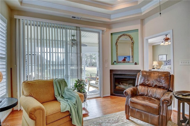 sitting room with a glass covered fireplace, visible vents, crown molding, and wood finished floors