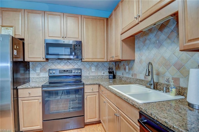 kitchen featuring appliances with stainless steel finishes, decorative backsplash, a sink, and light brown cabinetry