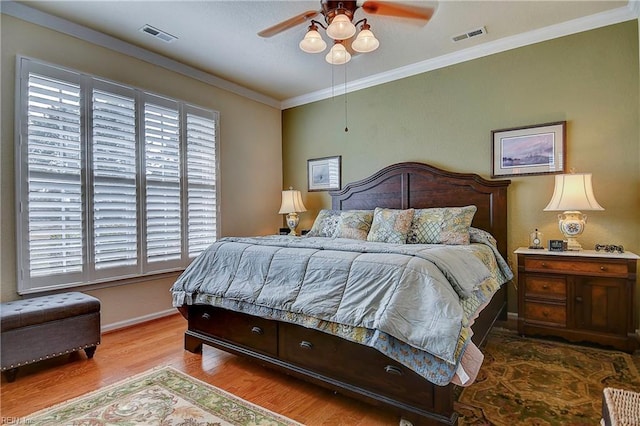 bedroom featuring ornamental molding, visible vents, baseboards, and wood finished floors