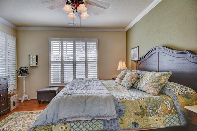 bedroom with ceiling fan, wood finished floors, visible vents, and crown molding