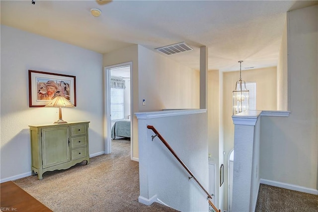 hall with a chandelier, a healthy amount of sunlight, visible vents, and an upstairs landing