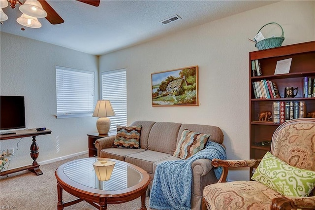 living area with carpet floors, visible vents, a textured wall, ceiling fan, and baseboards