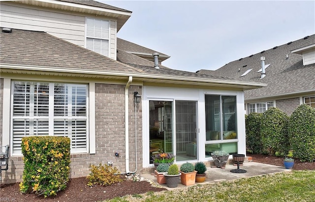 back of property with brick siding, a shingled roof, and a sunroom