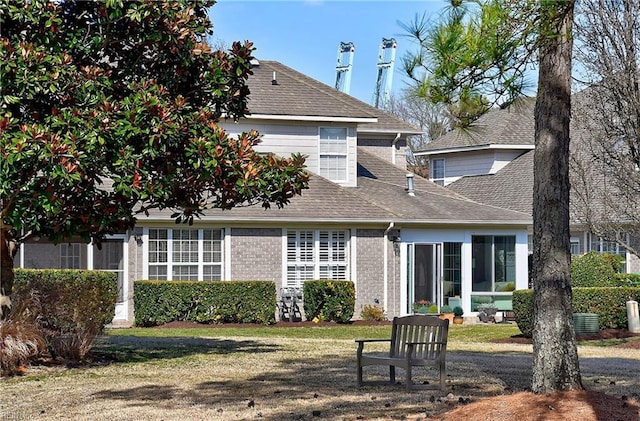 rear view of house featuring roof with shingles, brick siding, and a lawn