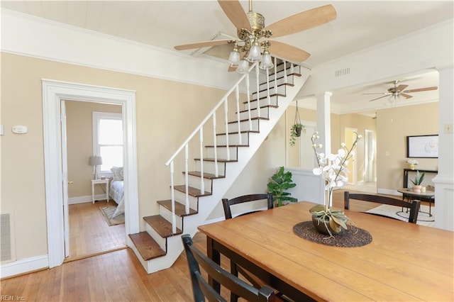 dining area featuring ornamental molding, a ceiling fan, light wood-type flooring, ornate columns, and stairs