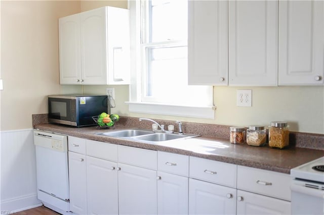 kitchen with white appliances, white cabinetry, a sink, and a wainscoted wall