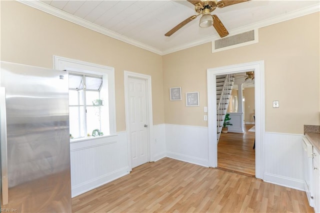 interior space with ceiling fan, crown molding, wainscoting, and light wood-style floors