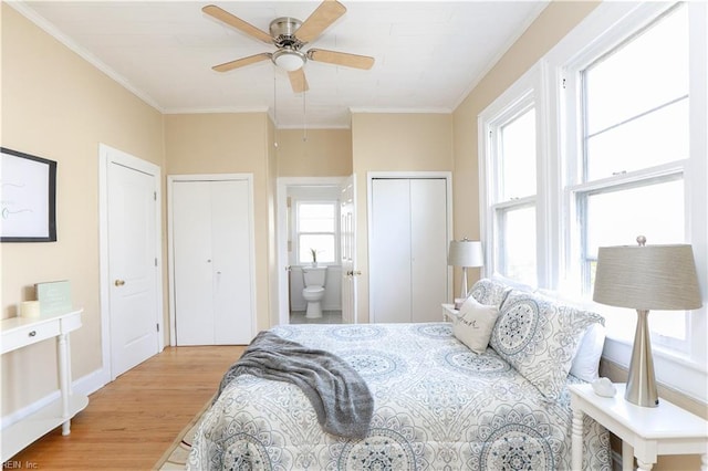 bedroom with ceiling fan, connected bathroom, light wood finished floors, two closets, and crown molding