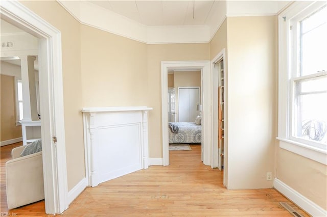 hallway featuring plenty of natural light, light wood-style flooring, visible vents, and crown molding