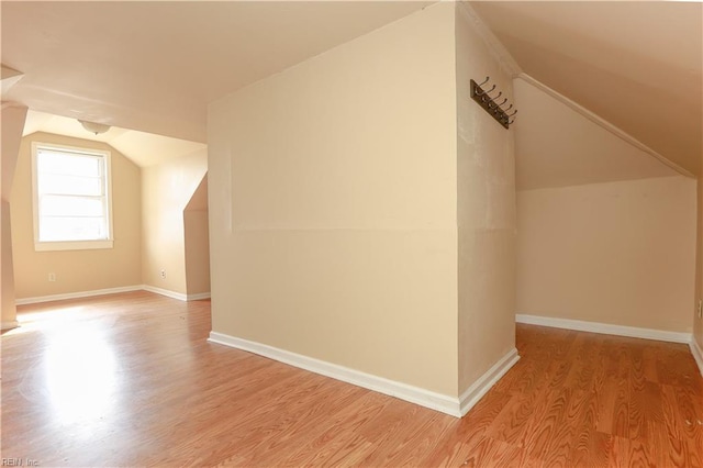 additional living space featuring light wood-type flooring, vaulted ceiling, and baseboards