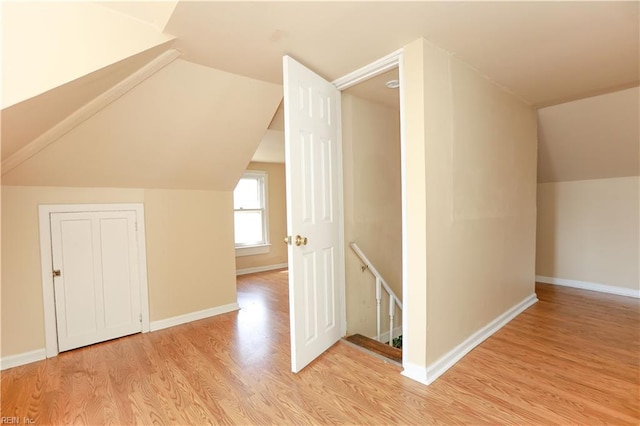 additional living space with baseboards, lofted ceiling, and light wood-style floors