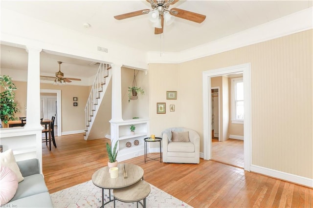 living room featuring ornate columns, stairway, light wood finished floors, and a ceiling fan