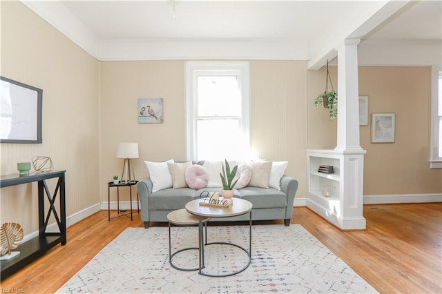 living room featuring baseboards, wood finished floors, and ornate columns