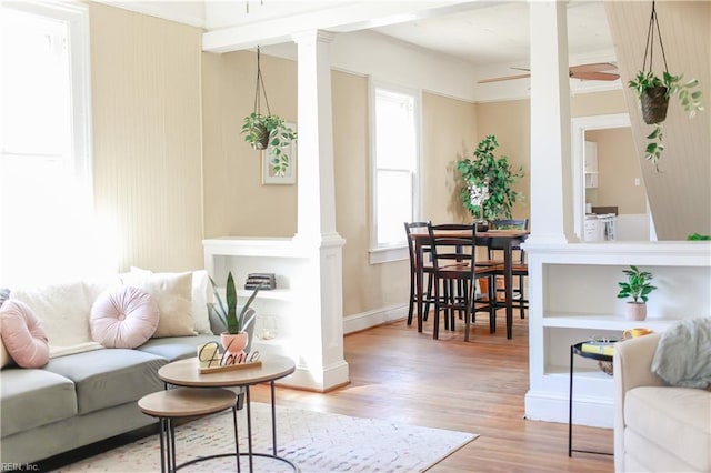 living area featuring decorative columns, baseboards, a ceiling fan, and wood finished floors