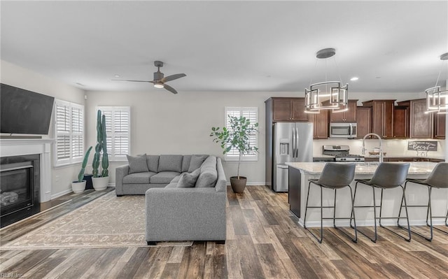 living room featuring ceiling fan, dark wood-type flooring, a glass covered fireplace, and a healthy amount of sunlight