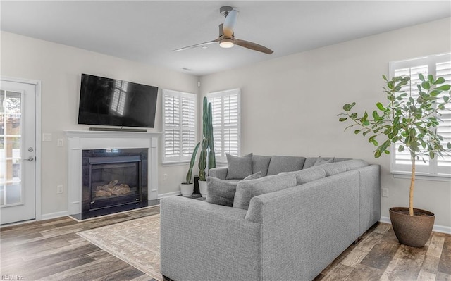 living area with baseboards, a premium fireplace, a ceiling fan, and wood finished floors