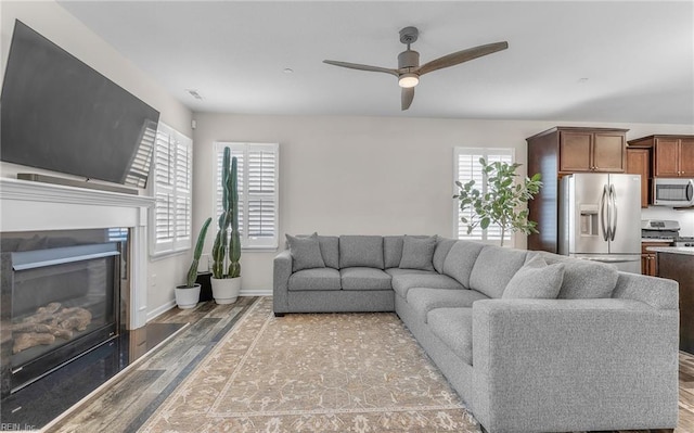 living room with baseboards, visible vents, a ceiling fan, a glass covered fireplace, and wood finished floors