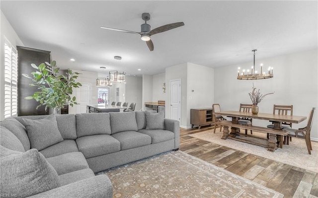 living area with ceiling fan with notable chandelier, baseboards, recessed lighting, and wood finished floors