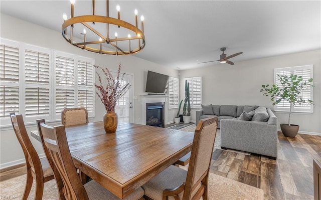 dining area featuring ceiling fan, a fireplace, baseboards, and wood finished floors