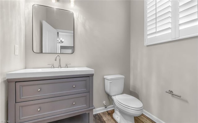 half bath featuring baseboards, vanity, toilet, and wood finished floors