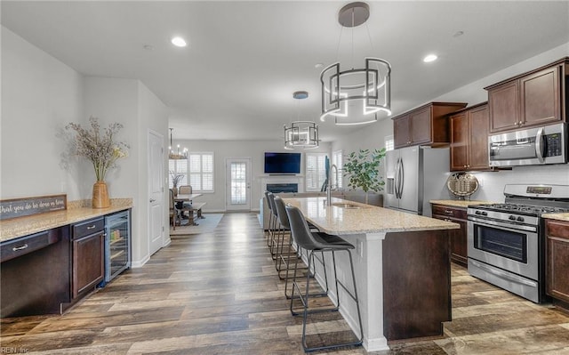 kitchen with beverage cooler, wood finished floors, stainless steel appliances, a fireplace, and a chandelier