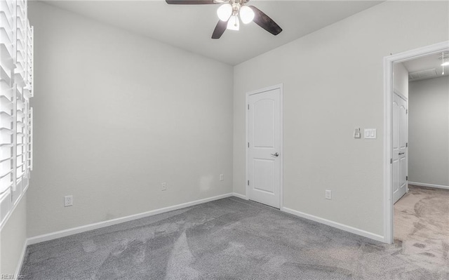 carpeted spare room with attic access, baseboards, and a ceiling fan