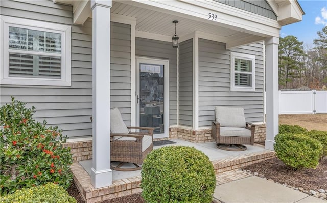 doorway to property with stone siding, fence, and a porch