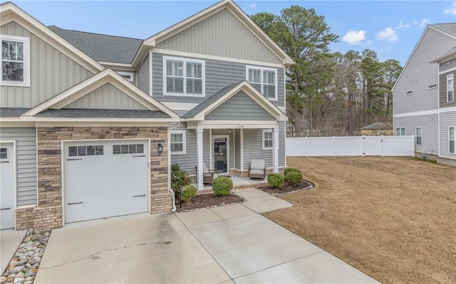 view of front of home featuring a garage, stone siding, fence, a porch, and board and batten siding