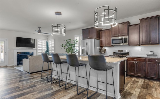 kitchen with a fireplace, a breakfast bar area, tasteful backsplash, appliances with stainless steel finishes, and dark wood-type flooring