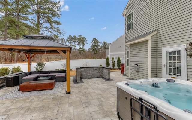 view of patio / terrace with a hot tub, a gazebo, fence, and an outdoor living space with a fire pit