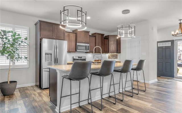 kitchen with backsplash, appliances with stainless steel finishes, wood finished floors, a chandelier, and a kitchen bar