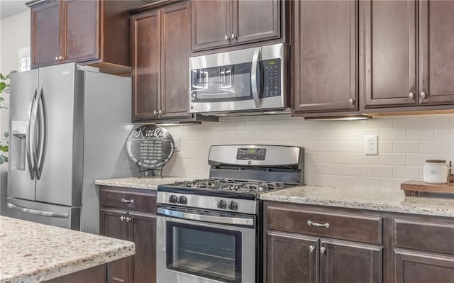 kitchen with light stone countertops, tasteful backsplash, appliances with stainless steel finishes, and dark brown cabinets