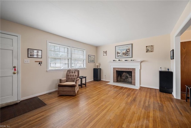 living area featuring a brick fireplace, wood-type flooring, and baseboards