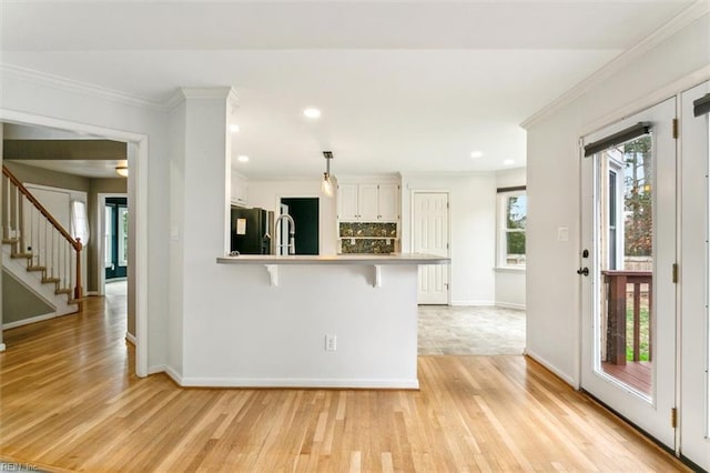 kitchen with a peninsula, white cabinets, crown molding, and freestanding refrigerator