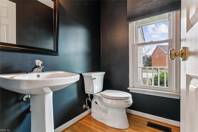 half bathroom with toilet, wood finished floors, visible vents, and baseboards