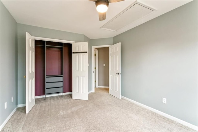 unfurnished bedroom with light carpet, a closet, attic access, and baseboards