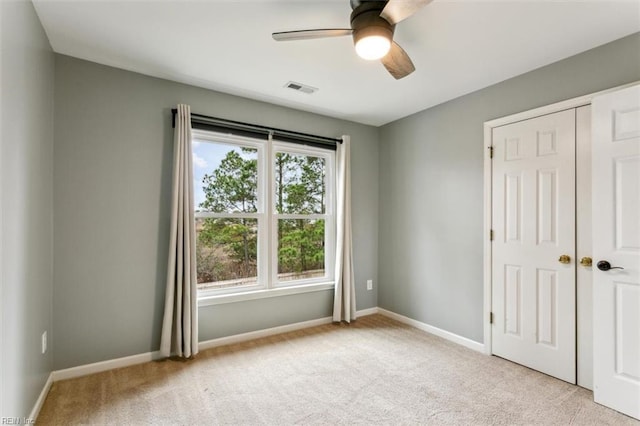 empty room featuring a ceiling fan, light colored carpet, visible vents, and baseboards