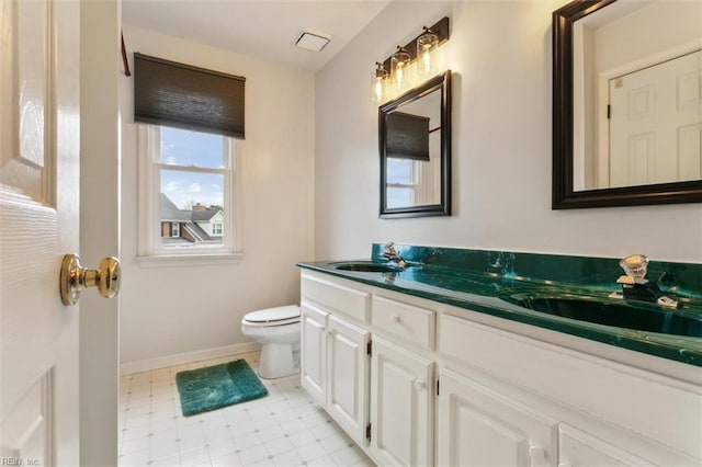 bathroom with toilet, double vanity, baseboards, and a sink