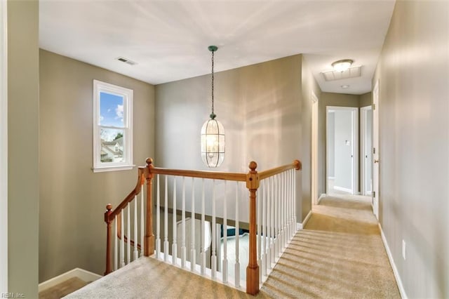 hall with carpet flooring, visible vents, baseboards, and an upstairs landing