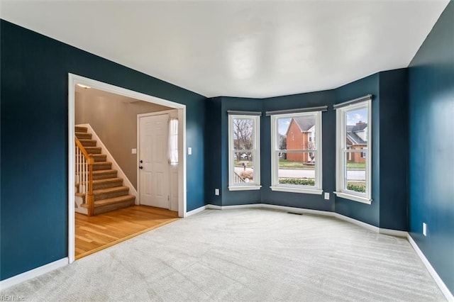 carpeted empty room featuring stairway, visible vents, and baseboards