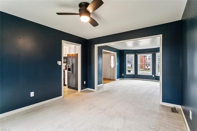 spare room featuring a ceiling fan, light carpet, visible vents, and baseboards