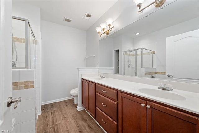 full bathroom featuring double vanity, visible vents, a sink, a shower stall, and wood finished floors