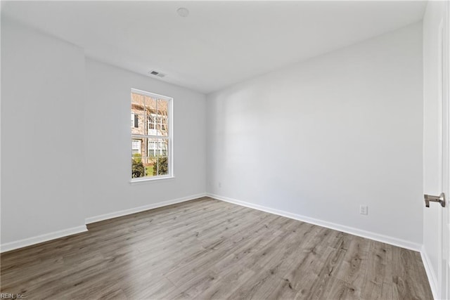 spare room featuring baseboards, visible vents, and wood finished floors