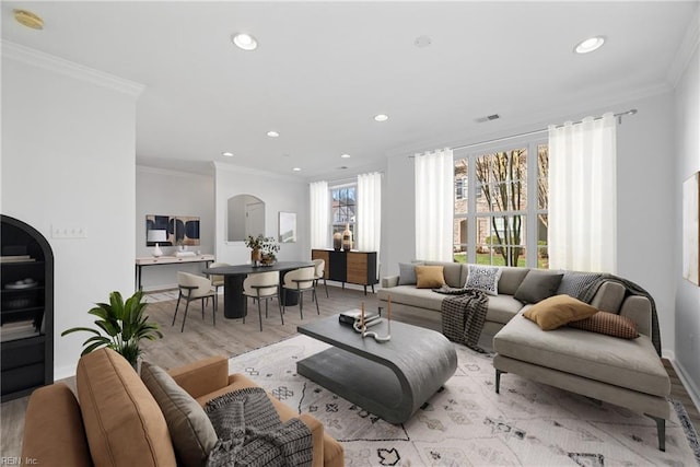 living room with light wood finished floors, visible vents, arched walkways, and crown molding