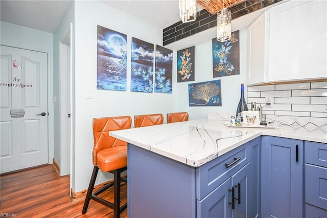 kitchen with dark wood-style floors, light stone counters, decorative backsplash, a peninsula, and a kitchen breakfast bar